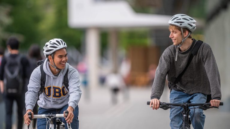 Two individuals biking on the UBC campus and smiling.